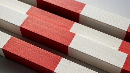 Close-up of several wooden square beams painted with alternating red and white sections, arranged in a diagonal pattern. Modern abstract architectural detail or industrial safety marking concept.