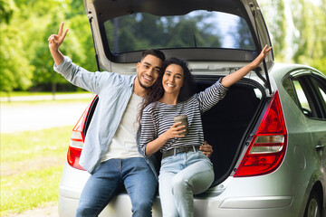 Happy lovers embracing and cheerfully smiling at camera while drinking coffee to go, raising hands...