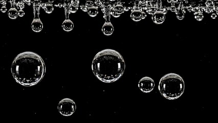 Close-up of clear water bubbles and droplets against a dark black background, showcasing various sizes and reflections.