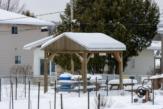 Canada, Quebec, 17 November 2025 : Snow covered wooden gazebo with benches and houses in background