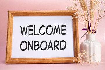 Welcome onboard symbol. Concept words Welcome onboard on beautiful wooden picture frame. Beautiful pink background with flower vase. Business and Welcome onboard concept. Copy space.