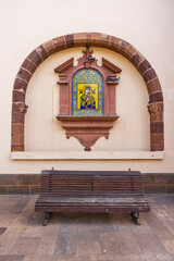 Religious ceramic tile image on church wall, arched stone niche above bench in La Laguna, San Cristobal de La Laguna, Tenerife.