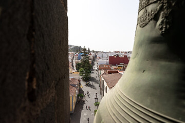 City view from church bell tower, bronze bell framing La Laguna street scene in San Cristobal de La Laguna, Tenerife.