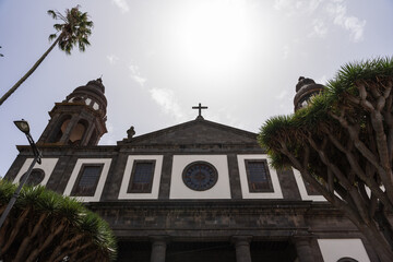 Cathedral facade with twin towers and cross, low angle view with palm and dragon trees in La Laguna, San Cristobal de La Laguna, Tenerife.