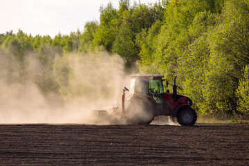 A red tractor plows the land, raising thick dust at sunset. A red tractor prepares the land with a plow. Preparing the land for a new crop plantation at sunset. © NastyaPhoto