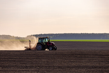 Obraz premium Tractor plowing field at sunset. Red tractor plowing, cultivating soil. Plow on plowed. Farm tractor on cultivated field for sowing seeds. Grain deal on field cultivation. Plowed field.