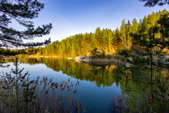 Still waters of a quarry lake and lush greenery surrounding it, creating a peaceful atmosphere. The fading light casts a gentle glow on the tranquil landscape.