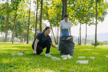 Two Asian women are picking up litter on the lawn in a park, participating in a daytime environmental cleanup.