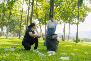 Two Asian women are picking up litter on the lawn in a park, participating in a daytime environmental cleanup.