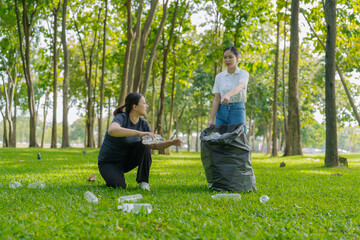 Two Asian women are picking up litter on the lawn in a park, participating in a daytime environmental cleanup.