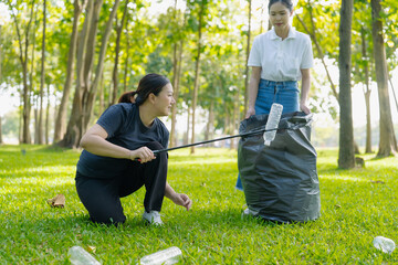 Two Asian women are picking up litter on the lawn in a park, participating in a daytime environmental cleanup.