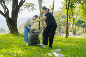 Two Asian women are picking up litter on the lawn in a park, participating in a daytime environmental cleanup.