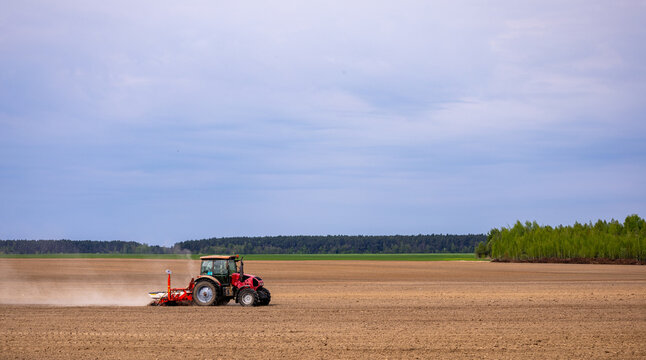 Farmer in tractor preparing farmland with seedbed for the next year. Powerful tractor at work, turning over soul on a vast farmland under a clear sky.