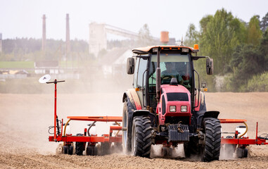 Fototapeta premium Tractor seeding soil with planter in agricultural field. Tractor drilling seeding crops at farm field. Agricultural activity. Tractor is equipped with seed planters to cultivate soil.