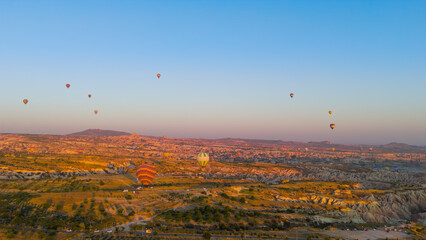 Goreme, Nevsehir, Turkey. Sunlit eroded plateau with intricate valley network and hot air balloons at sunrise over Cappadocia landscape with mountain silhouettes. Aerial View
