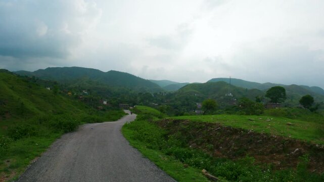 4K Wide angle view of road passing through green Sahyadri Hills at Rayta village in Udaipur, Rajasthan, India. Nature landscape. Monsoon clouds above green hills. Travel background.