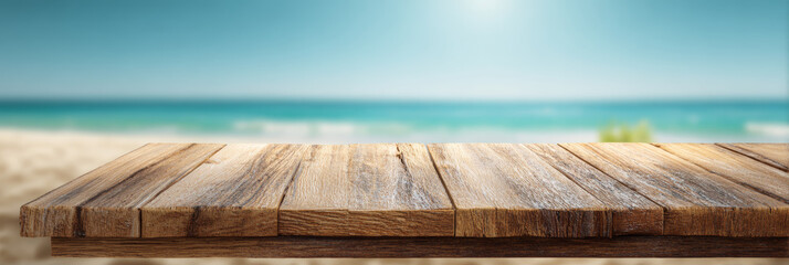 Empty wooden table top with visible natural grain and texture overlooking a blurred sandy beach with turquoise sea and sky in the background