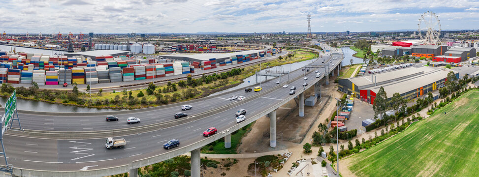 Aerial panorama view of an elevated freeway between sports fields and stacks of freight containers