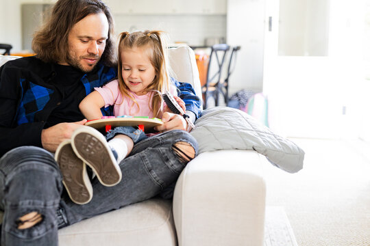 Father playing with a wooden clock with young daughter on the lounge
