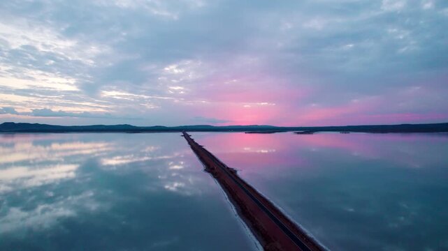 4K aerial view of beautiful road and salt water lake on both sides, connecting Khavda to Dholavira in Kutch, Gujarat, India. Road to heaven. Road trip. Clouds in sunset sky with infinite road.
