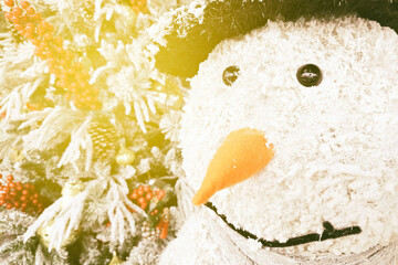 Snowman decoration with a carrot nose and hat next to a flocked Christmas tree.