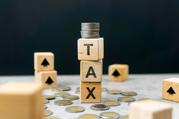 A wooden cube with the text TAX and a stack of coins, as well as an upward arrow representing...