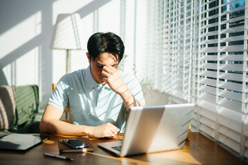Obraz premium Frustrated young businessman working on a laptop computer sitting at his working place in office