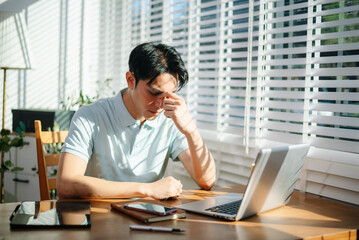 Frustrated young businessman working on a laptop computer sitting at his working place in office