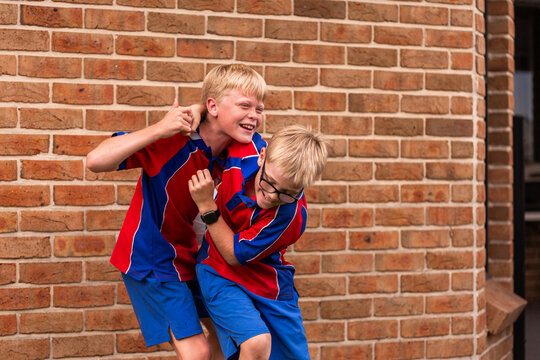 School aged children in uniform being silly wrestling together older brother and younger sibling