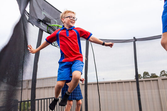 Happy siblings bouncing on trampoline playing ball game together after school