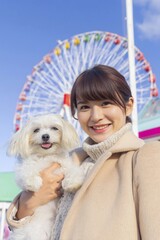 観覧車の前で愛犬を抱く笑顔の女性
