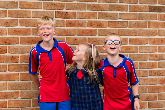 Happy group of three primary school kids laughing together with arms around each other