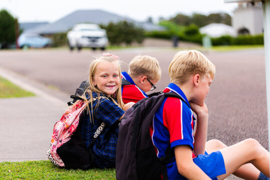 Group of young schoolkids sitting waiting for school bus on the edge of the road in suburban area
