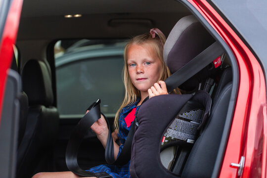 Young school student getting herself buckled into booster seat in car with lap and sash belt