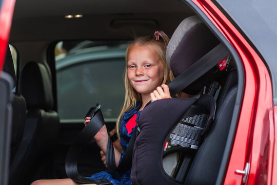 Young school student getting herself buckled into booster seat in car with lap and sash belt