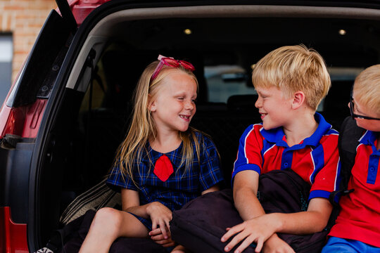 Happy school kid siblings looking at each other sitting in car boot ready for school drop off