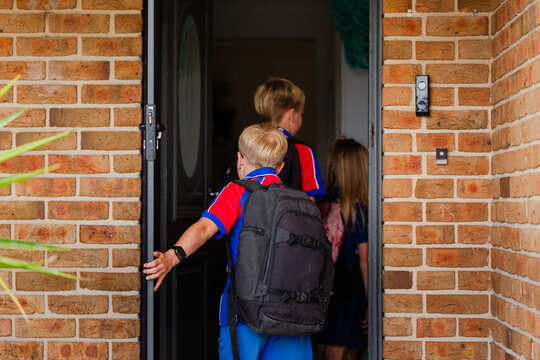 Primary aged children coming home from school walking through front door at home