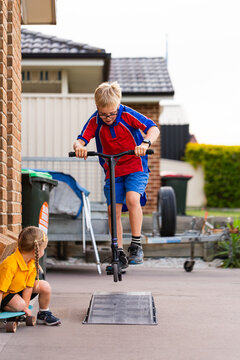 Australian schoolboy in uniform riding scooter doing tricks outside home after school