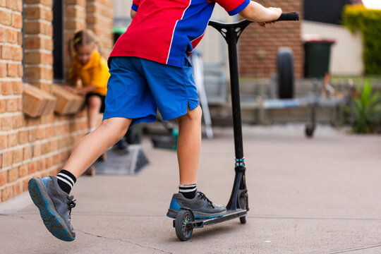 Australian schoolboy in uniform riding scooter around outside home after school