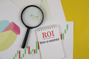 ROI Concept With Business Charts, Pie Diagram, And Magnifying Glass For Investment Analysis. isolated on a yellow surface.