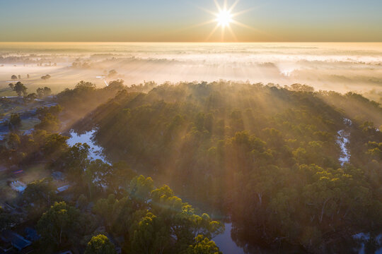 Aerial view of morning sunshine through thin fog over bushland along an inland river