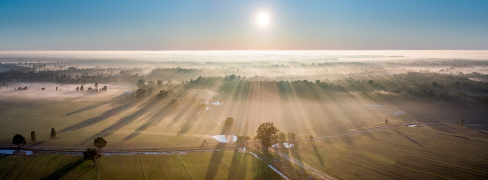 Aerial panorama view of sunshine through a layer of fog over a forest of farmland
