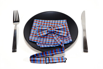 Elegant table setting with silverware and a black plate with vibrant bow tie closeup view on white...