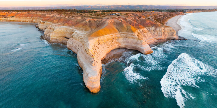Aerial panorama view of waves hitting an eroded point along a rugged coastline in golden lighting