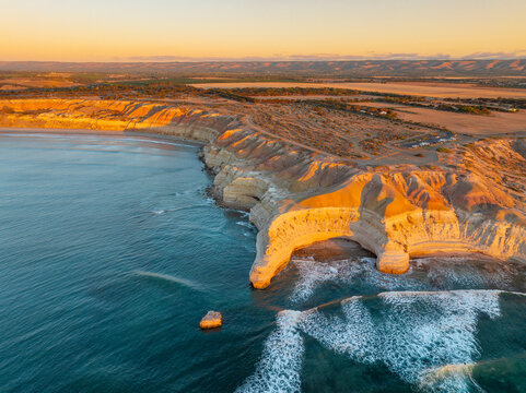 Aerial view of a crescent shaped cove along a rugged eroded coastline on golden evening light