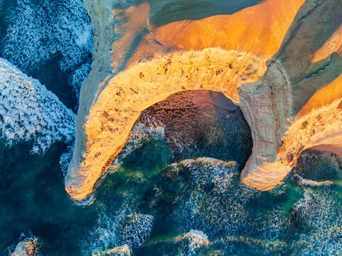 Aerial view of a crescent shaped cove along a rugged eroded coastline on golden evening light