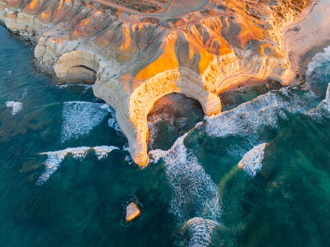 Aerial view of a crescent shaped cove along a rugged eroded coastline on golden evening light