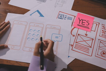 Close up ux developer and ui designer brainstorming about mobile app interface wireframe design on table with customer breif and color code at modern office.Creative digital development agency.