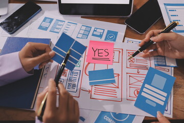 Close up ux developer and ui designer brainstorming about mobile app interface wireframe design on table with customer breif and color code at modern office.Creative digital development agency.