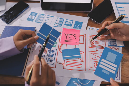 Close up ux developer and ui designer brainstorming about mobile app interface wireframe design on table with customer breif and color code at modern office.Creative digital development agency. - Powered by Adobe